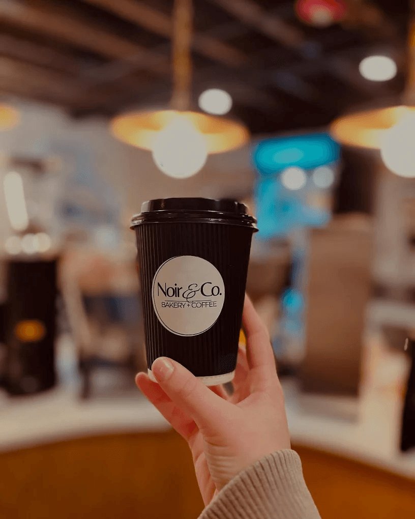 Hand holding a to-go coffee cup from Noir Bakery & Coffee Co.